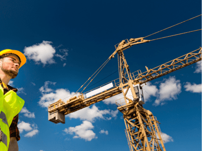 Man on a construction building site looking up at a yellow crane