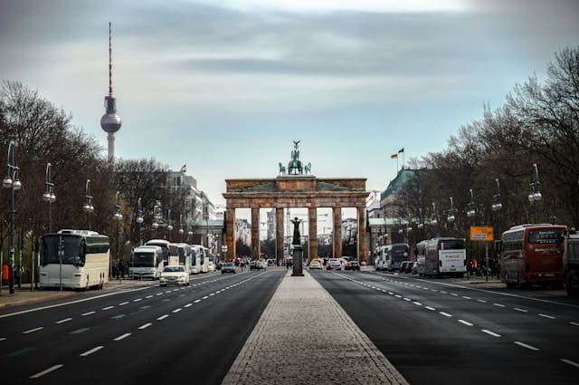 Road in the evening light, in the enctre the Brandneburger Tor, in the background the Fernsehturm of Berlin. It is cloudy and no cars on the roads.